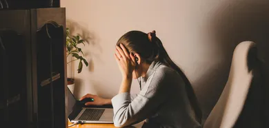 Frau mit Kopfhörern sitzt frustriert vor einem Laptop am Schreibtisch – Symbolbild für psychologische Hürden beim Lernen im Erwachsenenalter